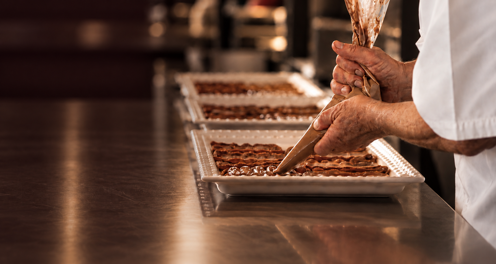 Chocolatier piping tempered chocolate onto trays in a professional kitchen
